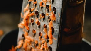 A Grater and Grated Carrots on a Bowl