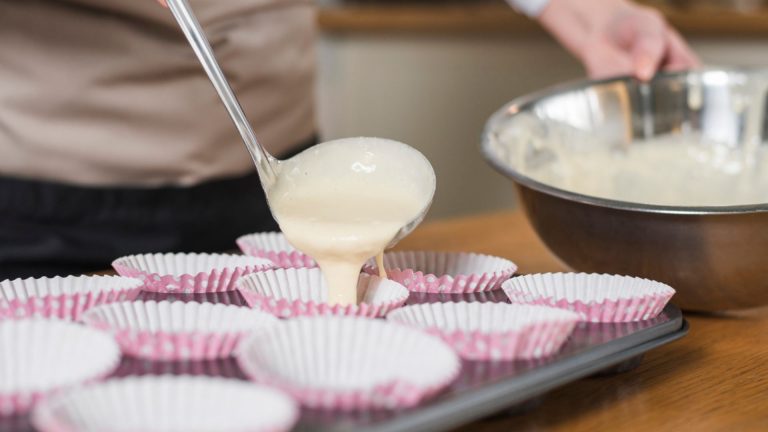 Close-up of woman pouring cake batter in the cupcake case with ladle