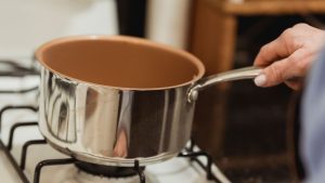 Crop unrecognizable housewife placing saucepan on stove