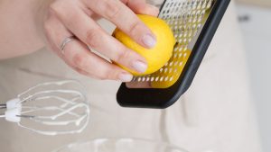 Crop woman grating lemon zest while cooking in kitchen