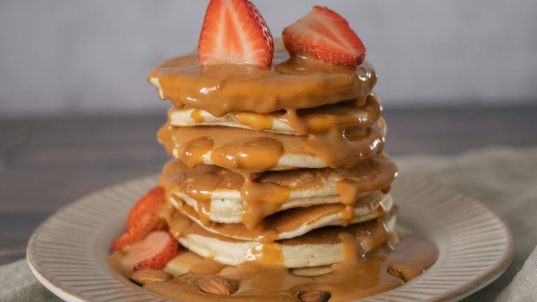 Delicious pancakes with caramel syrup and strawberries served on plate