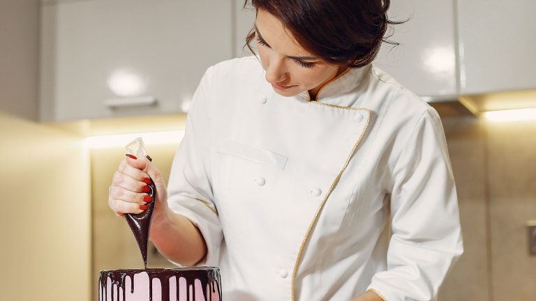 Female confectioner decorating cake with chocolate in contemporary kitchen