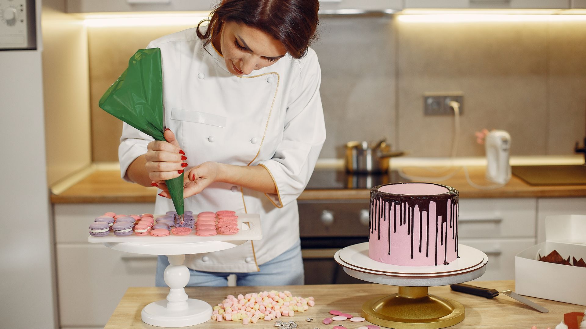 Female pastry chef adding cream on macaroons shells in modern bakery...