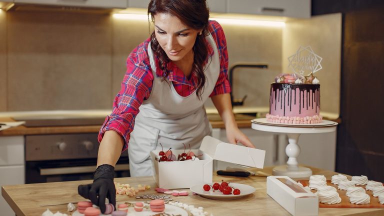 Focused woman decorating cake with macaroons in kitchen