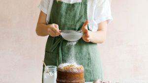 Woman Sprinkling Confectioner's Sugar on Baked Cake