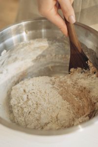 A Person Mixing the Dough Using a Wooden Spatula in a Stainless Bowl